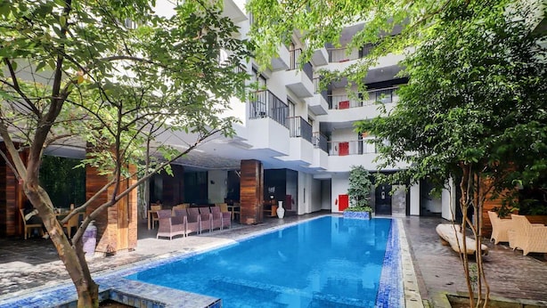 Une piscine intérieure aux bords carrelés, entourée d’arbres et bordée d’un immeuble à plusieurs étages doté de balcons.