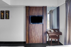 A hotel room with a wooden accent wall, a flat-screen TV mounted on it, a desk with a telephone, and a chair. - Palette Hotel Seminyak (Seminyak)