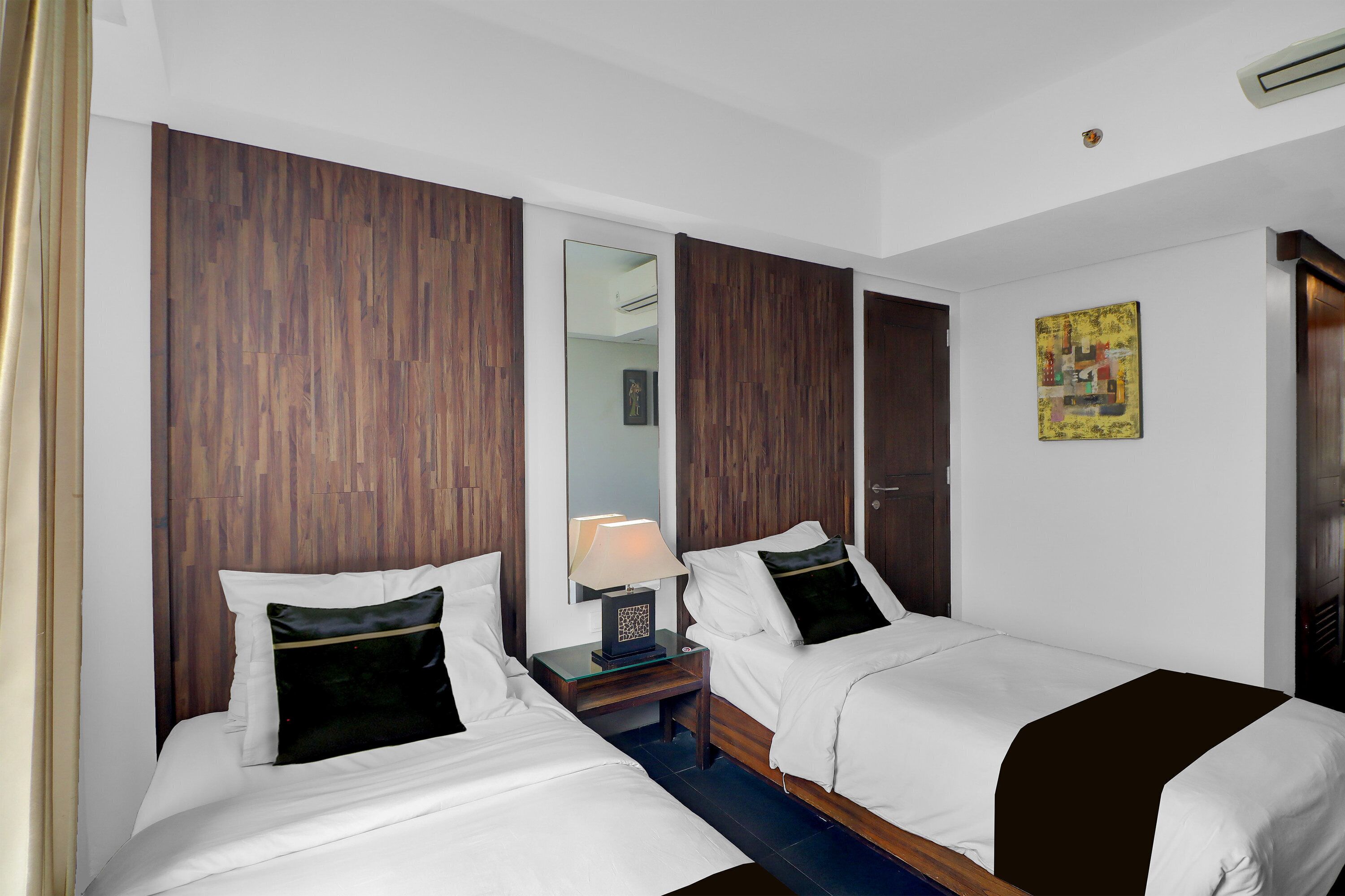 Une chambre d’hôtel avec deux lits, des têtes de lit en bois, une table de chevet avec une lampe, un miroir et un tableau au mur.