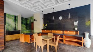 Un intérieur moderne comprenant un coin repas, un mur noir orné d’une horloge et un grand vase rempli de fleurs.