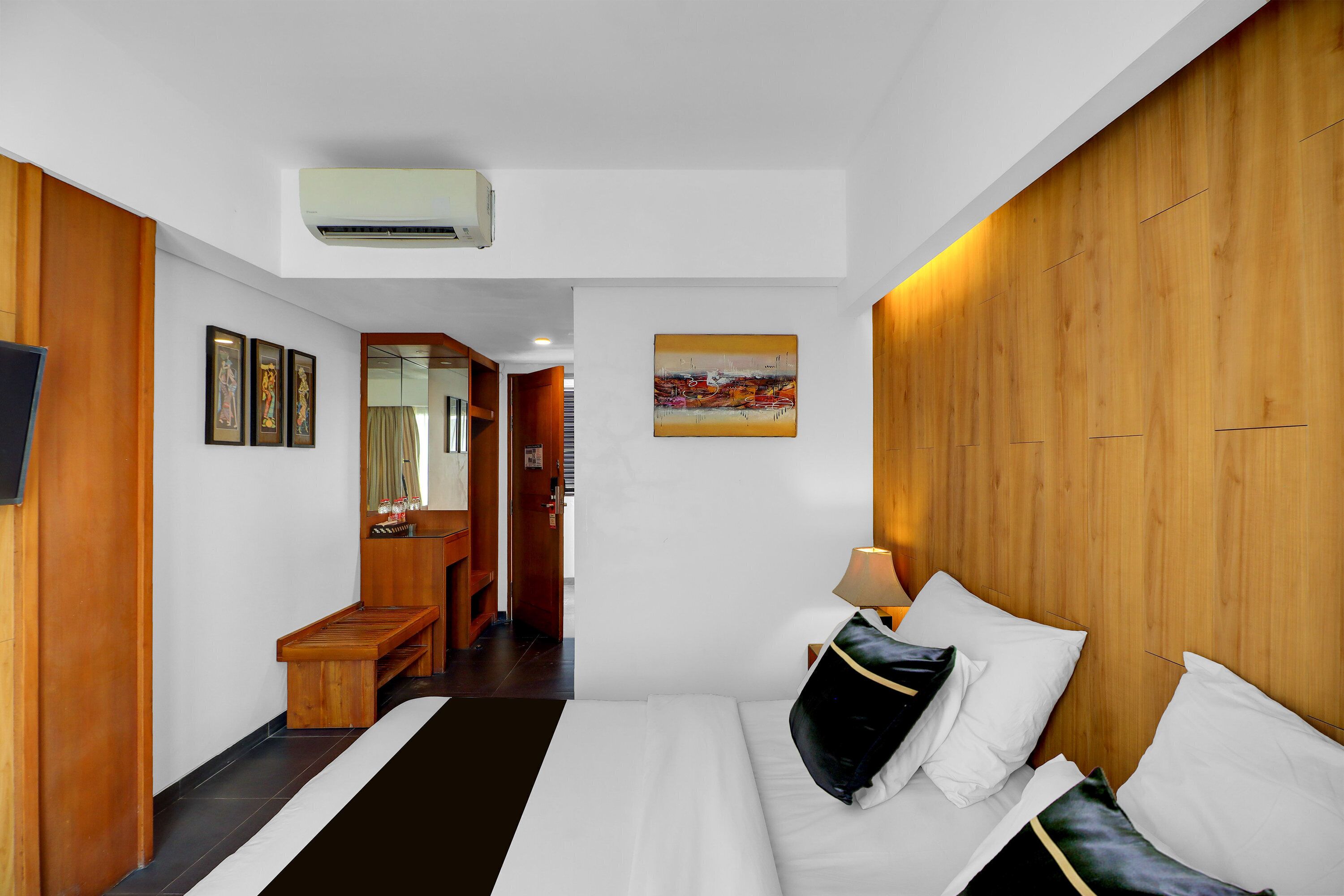 A hotel room with a bed, a desk, a mirror, and a painting on the wall.