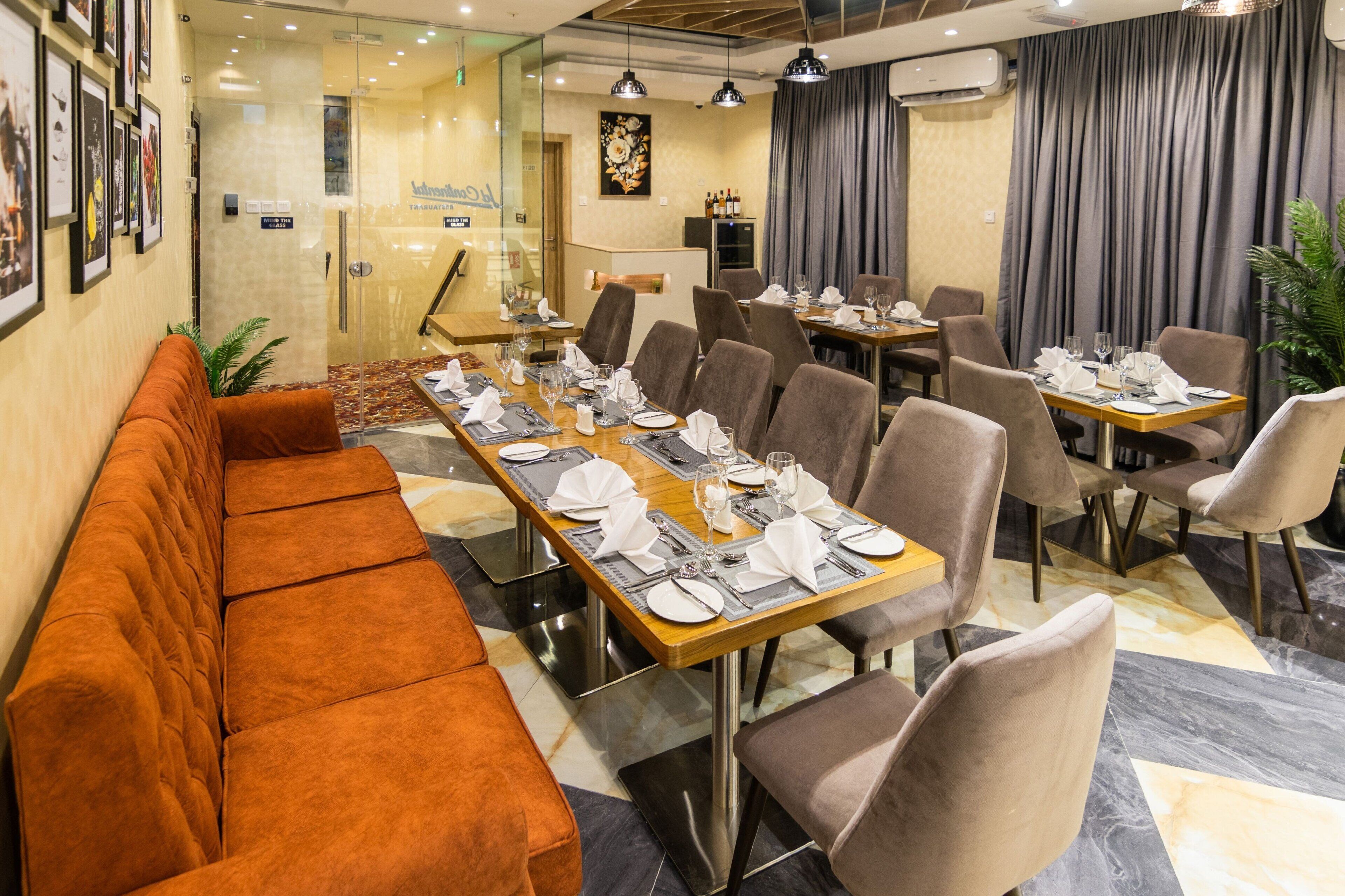 A restaurant with a long wooden table set for dining, cushioned seating, and a modern interior design.
