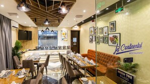 Un restaurante con una decoración moderna, que presenta una larga mesa de comedor con múltiples sillas, un sofá naranja acolchado y una pared decorada con cuadros.