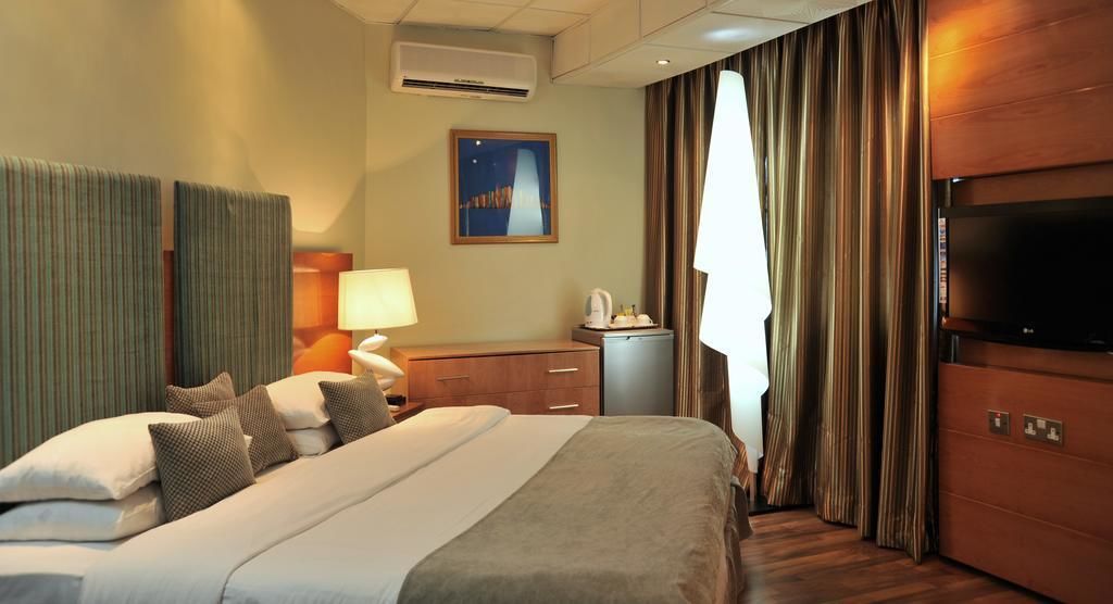 Une chambre d’hôtel avec un grand lit, un bureau avec une lampe, une télévision et une fenêtre avec des rideaux.