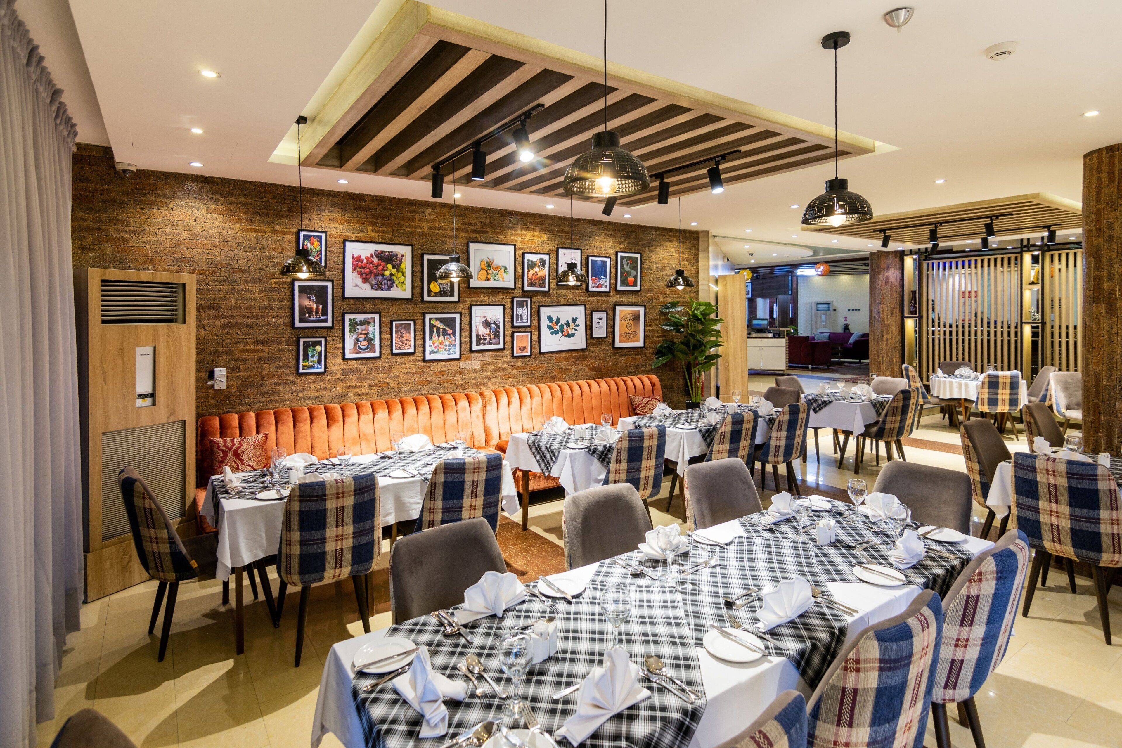 A restaurant with multiple tables set for dining, a brick wall with framed pictures, and a modern ceiling design.