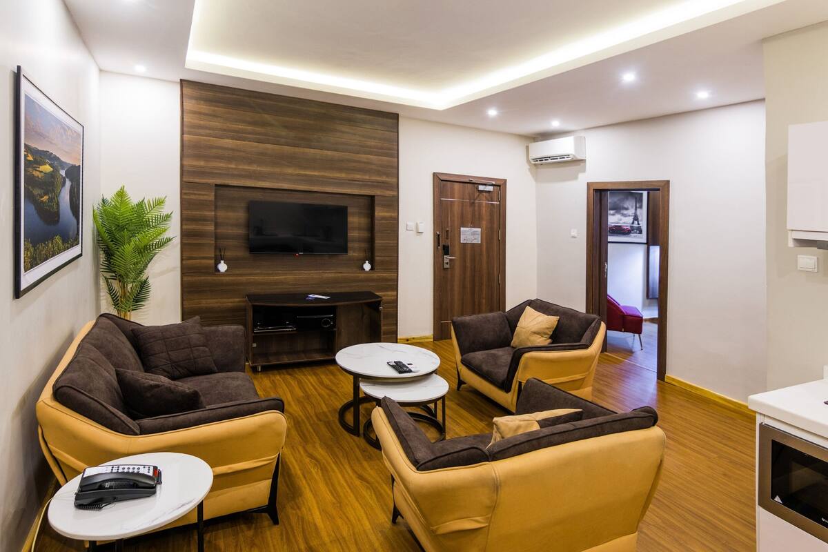 A modern living room with sofas, a coffee table, a flat-screen TV, and a potted plant.