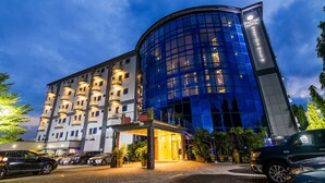 Un hotel con fachada de vidrio moderna, una entrada bien iluminada y un estacionamiento con varios autos.