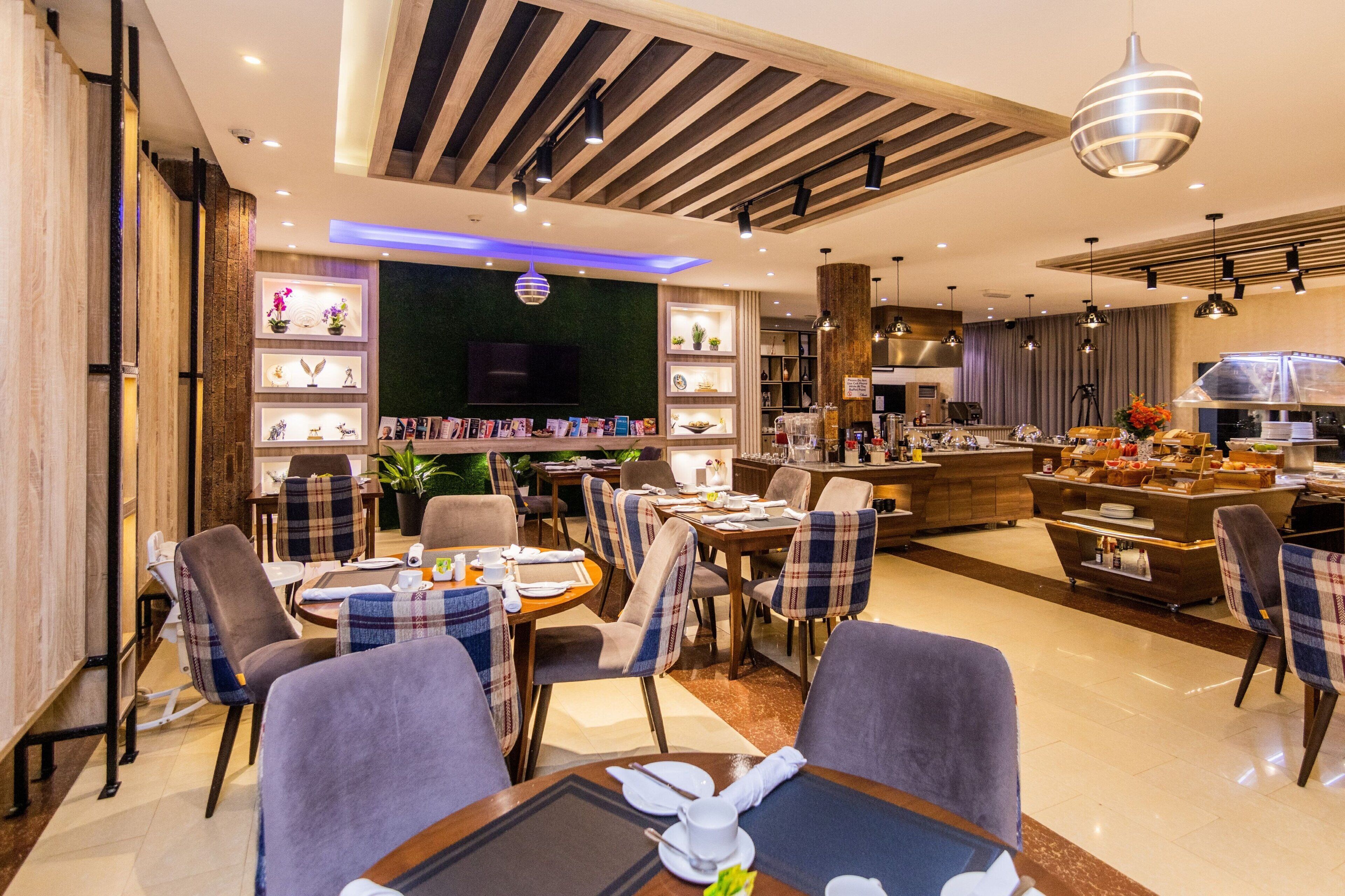 A modern hotel lobby with a dining area, a kitchen, and a TV screen.