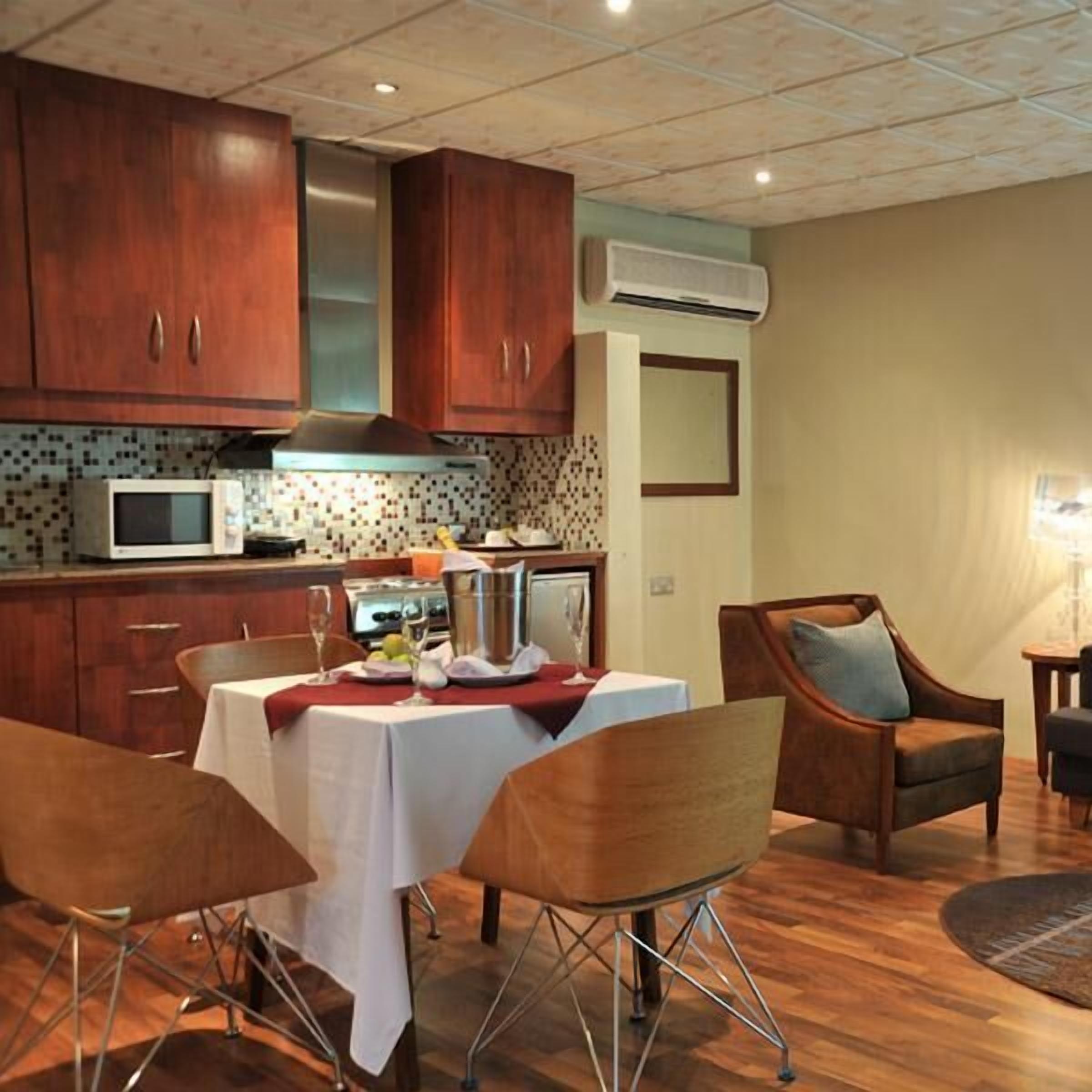 A compact kitchen with wooden cabinets, a microwave, and a dining area with a table set for two.