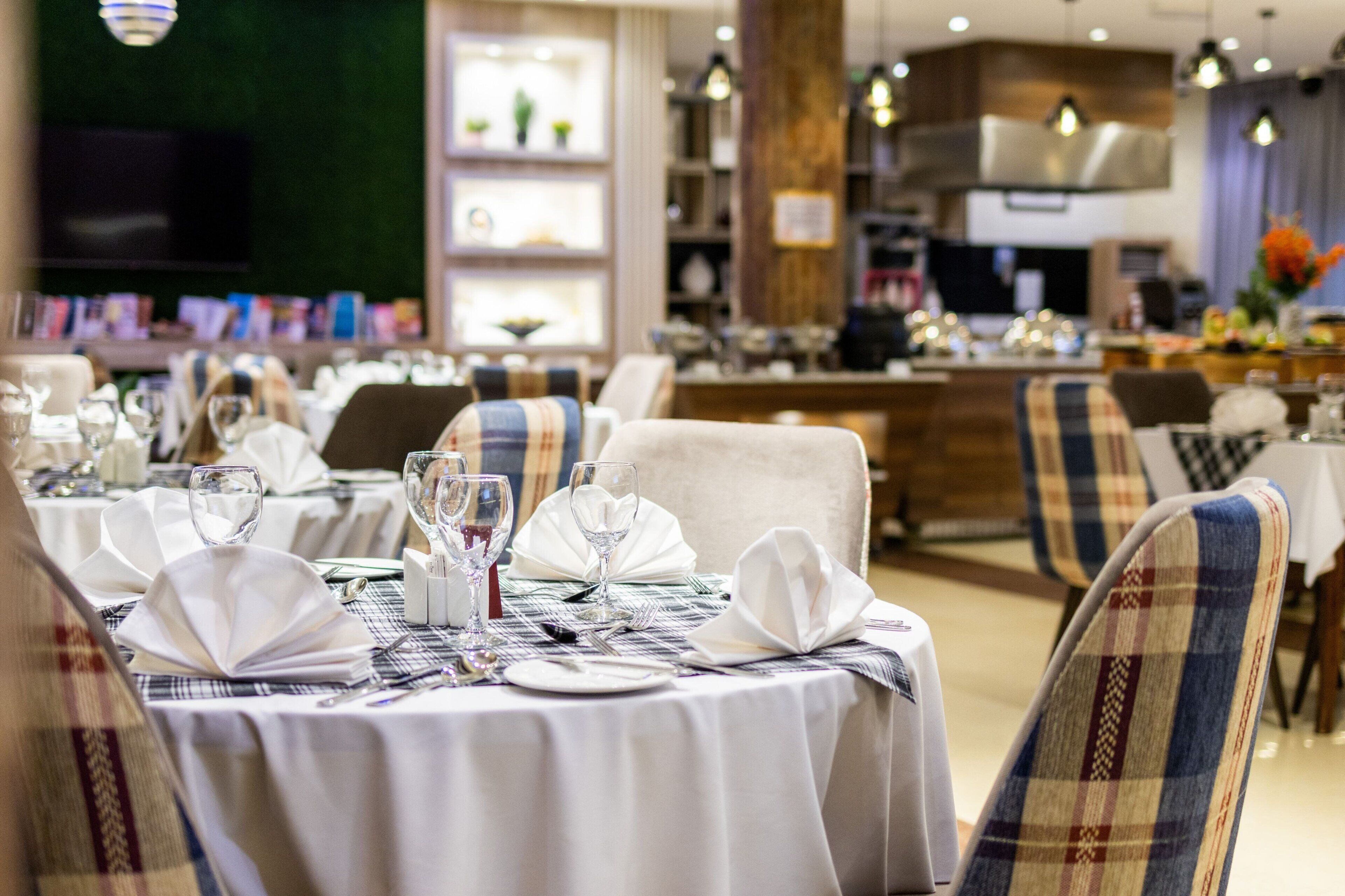 A restaurant with round tables set for dining, featuring white tablecloths and plaid chairs.