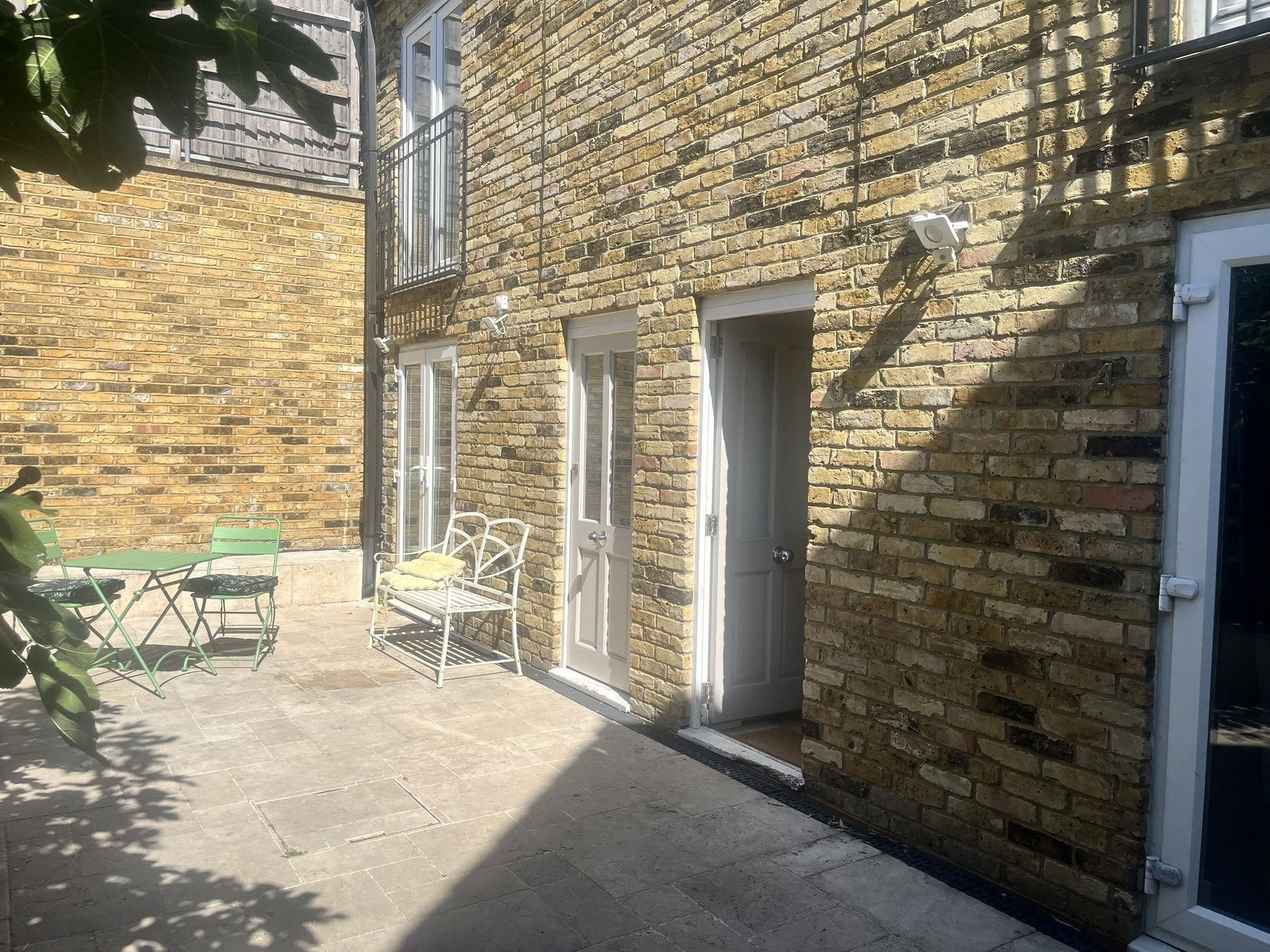 A brick building with a patio area, a green table and chairs, and a white door.