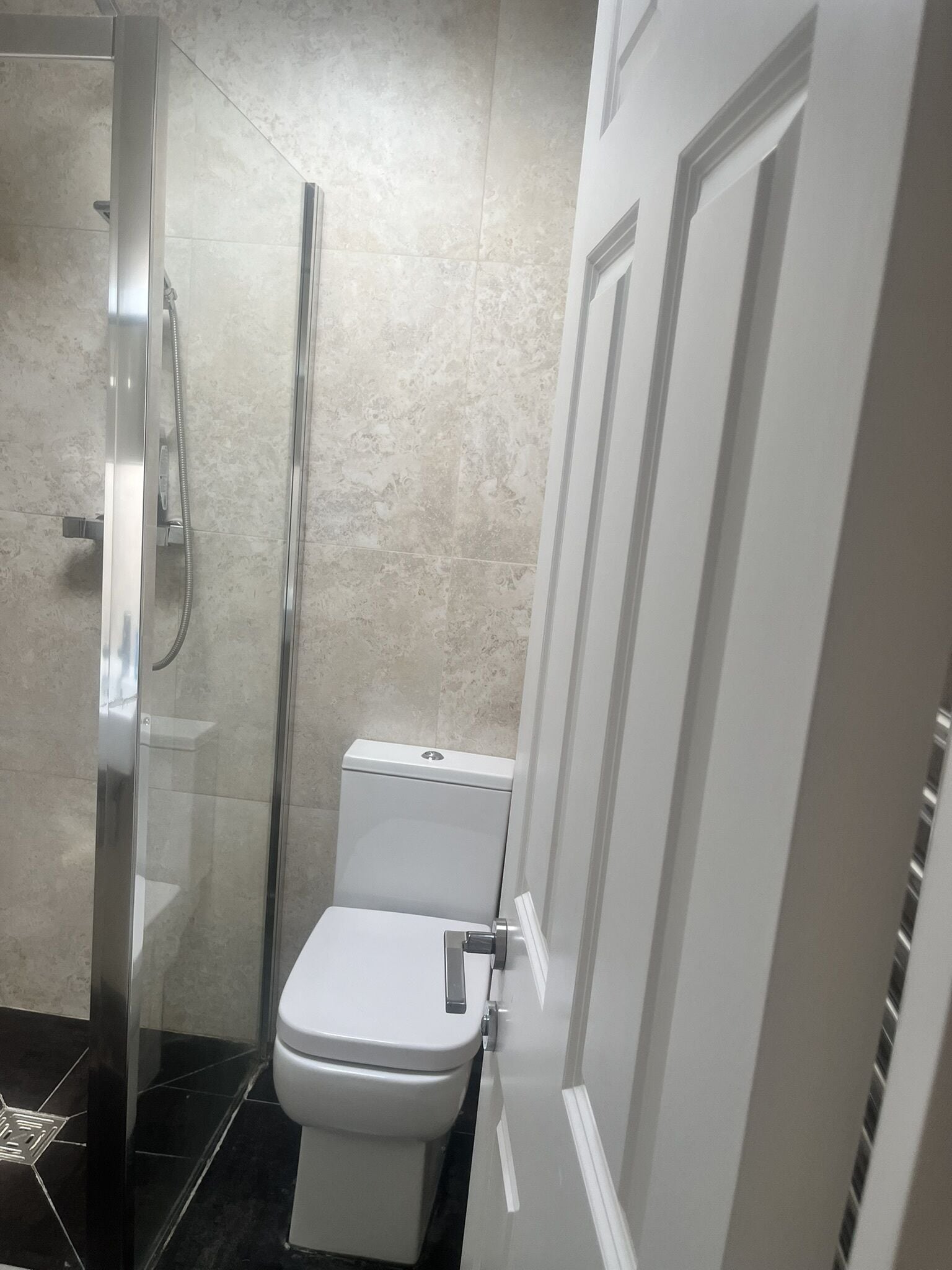 Une salle de bain avec une douche à parois de verre, des toilettes blanches et une porte dotée d’une poignée.