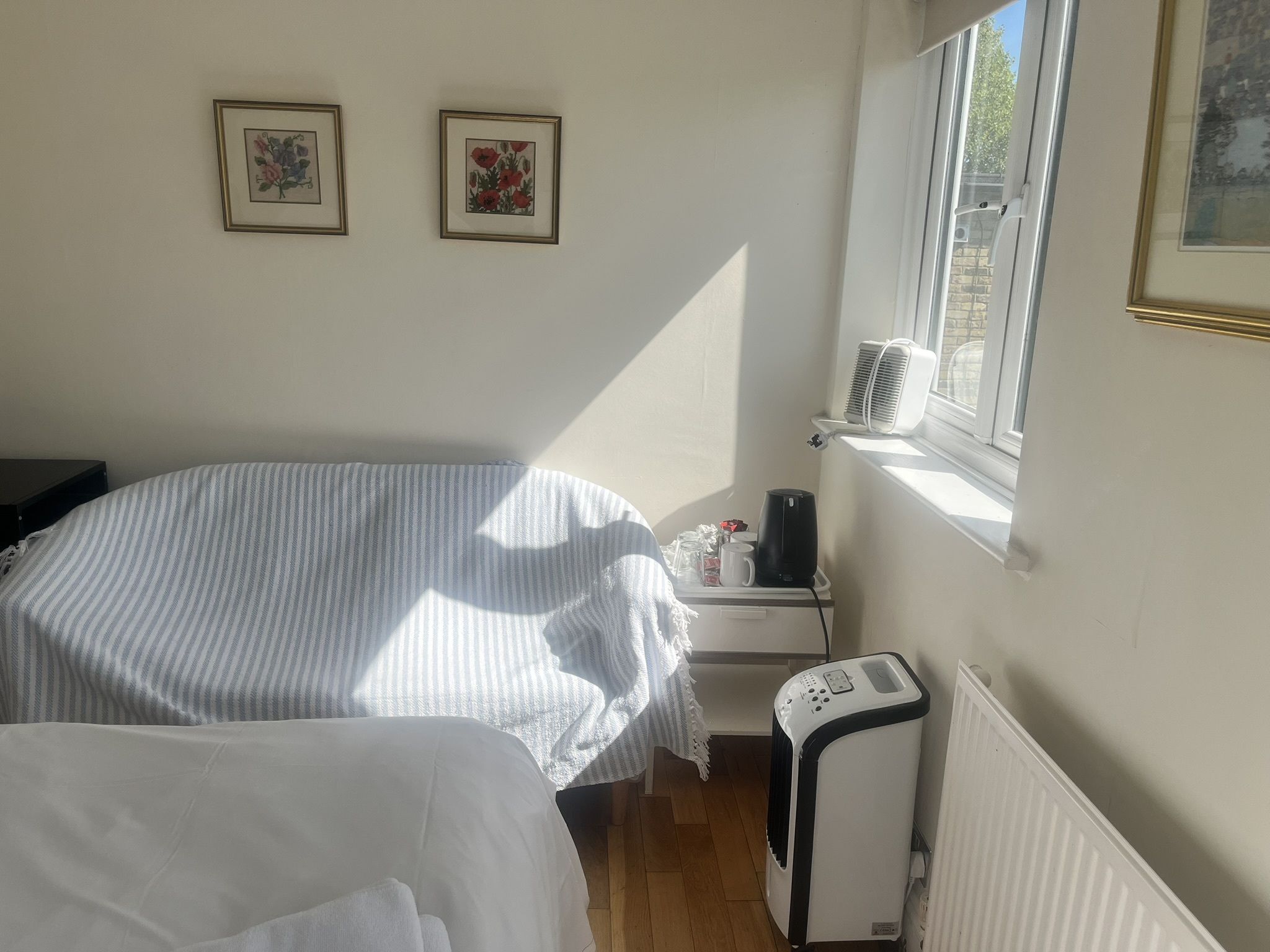 Un dormitorio con una cama, una mesita de noche con lámpara, un radiador y una ventana con aire acondicionado.