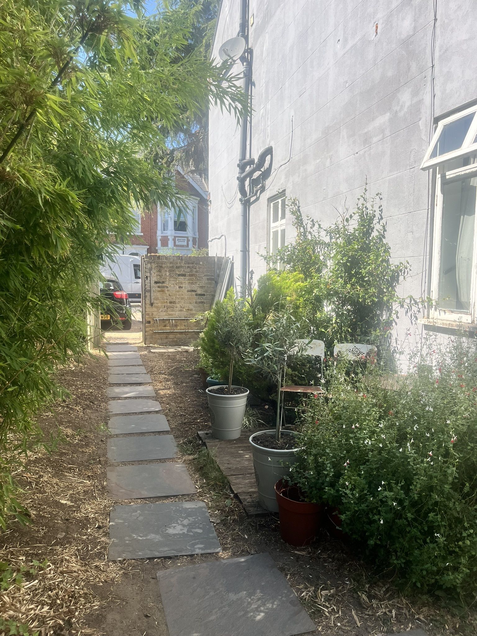 A narrow stone pathway leading to a building with a brick facade and a window.