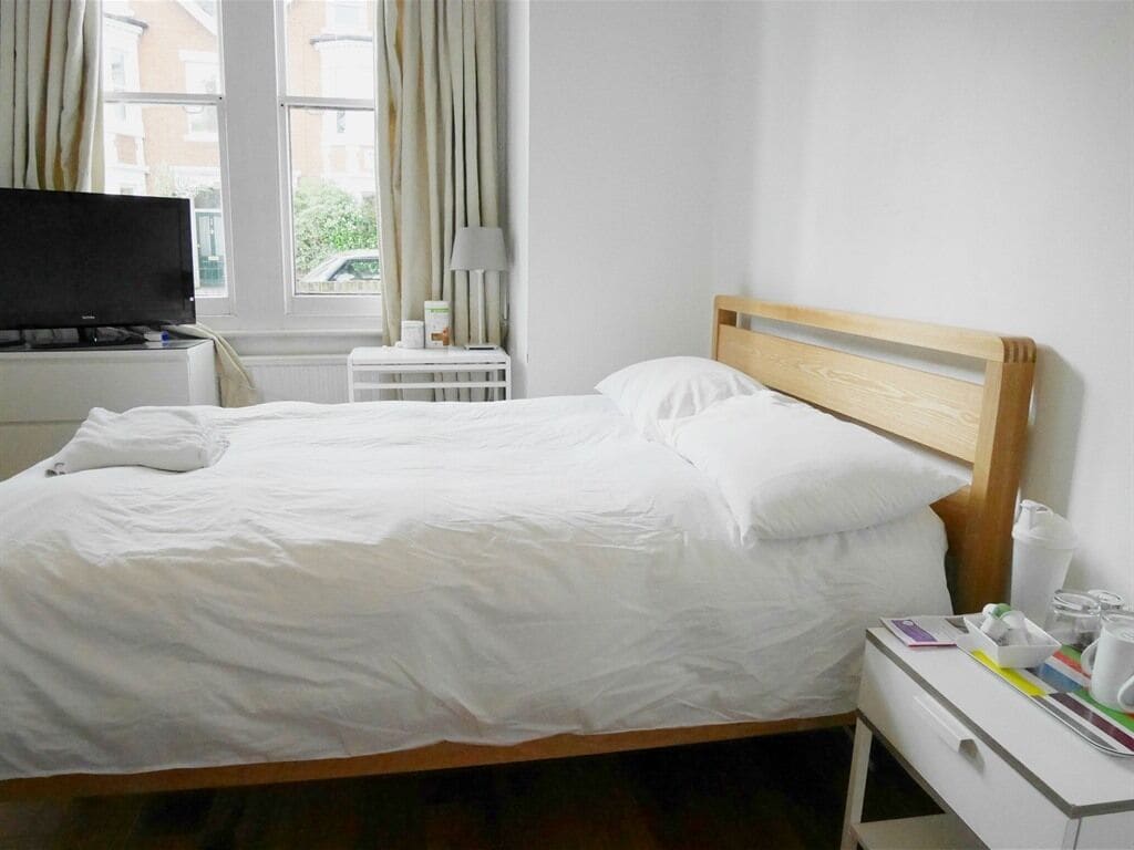 A neatly made bed with white linens, a wooden headboard, a bedside table with a lamp, and a small white cabinet.