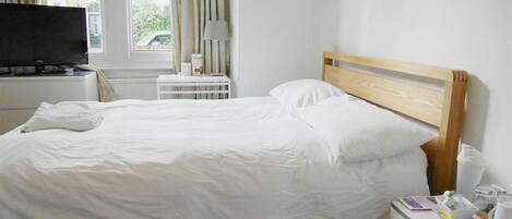 A neatly made bed with white linens, a wooden headboard, a bedside table with a lamp, and a small white cabinet.