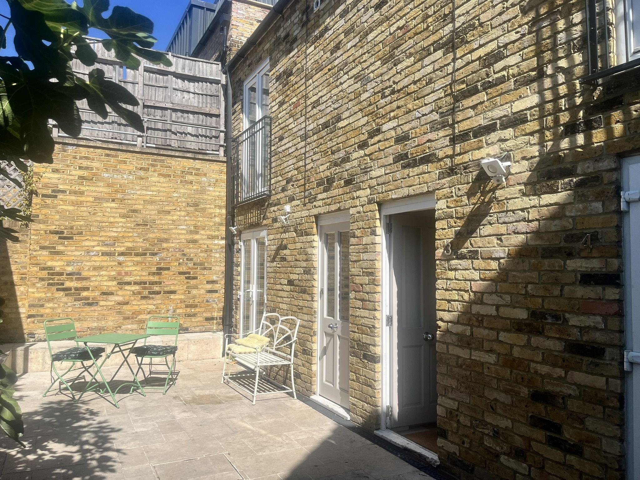 A courtyard with a brick building, a wooden fence, and a metal table with chairs.