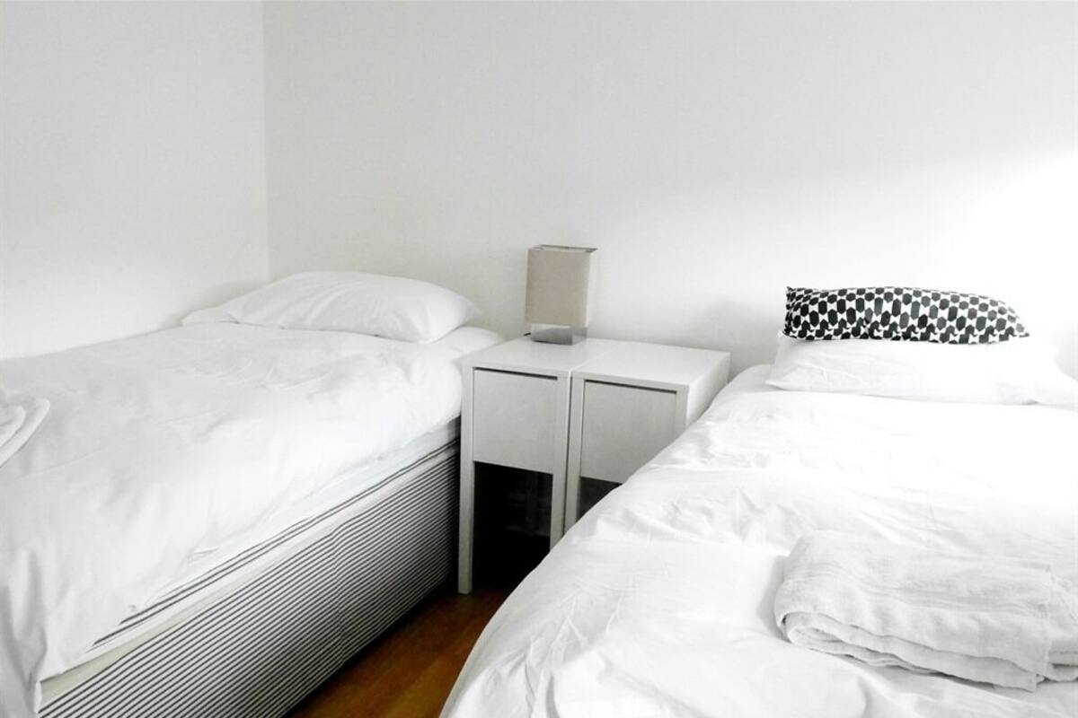 A hotel room with two single beds, a nightstand with a lamp, and a patterned pillow.