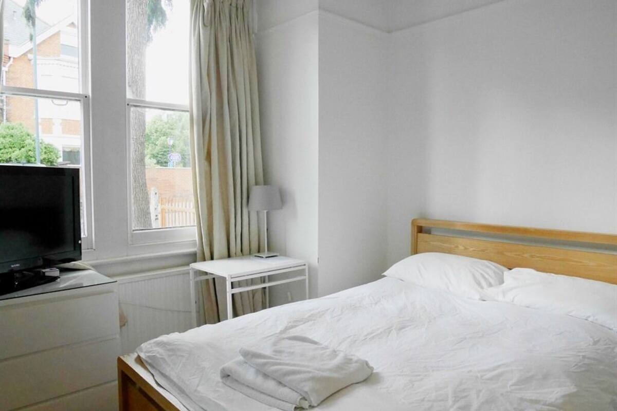 A hotel room with a bed, a TV on a dresser, a lamp, and a window with curtains.