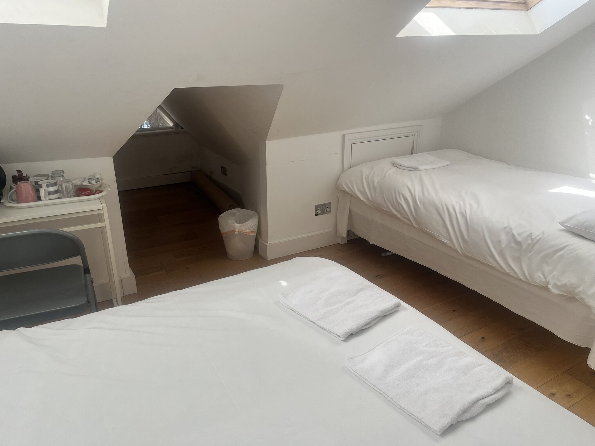 A small, tidy room with two beds, a desk, and a trash bin.