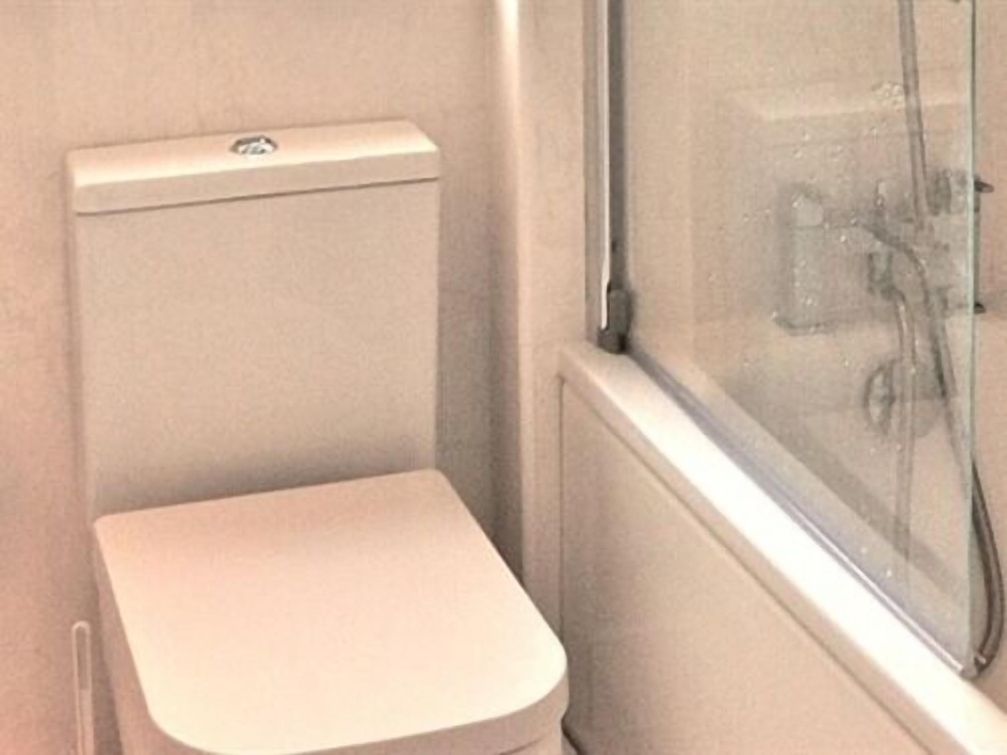 A small, enclosed bathroom with a toilet, a window, and a visible shower area.