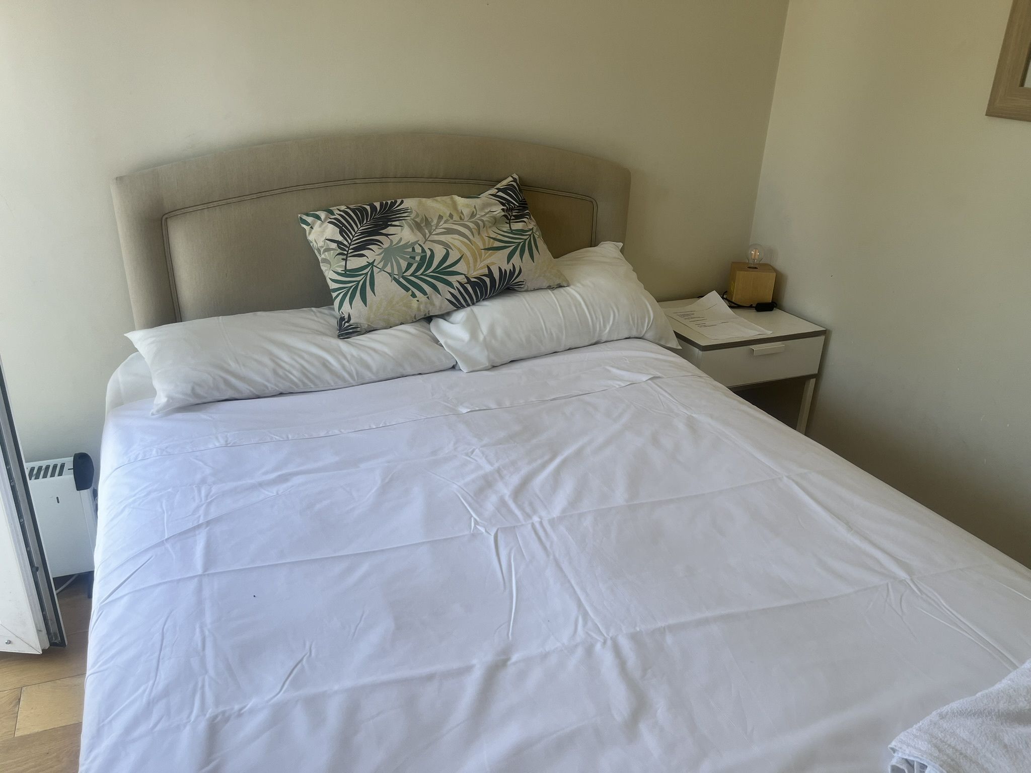 A neatly made bed with white linens and a single decorative pillow with a leaf pattern.