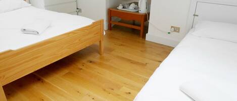 Un dormitorio con dos camas de madera, una mesita de noche y un taburete pequeño de madera.