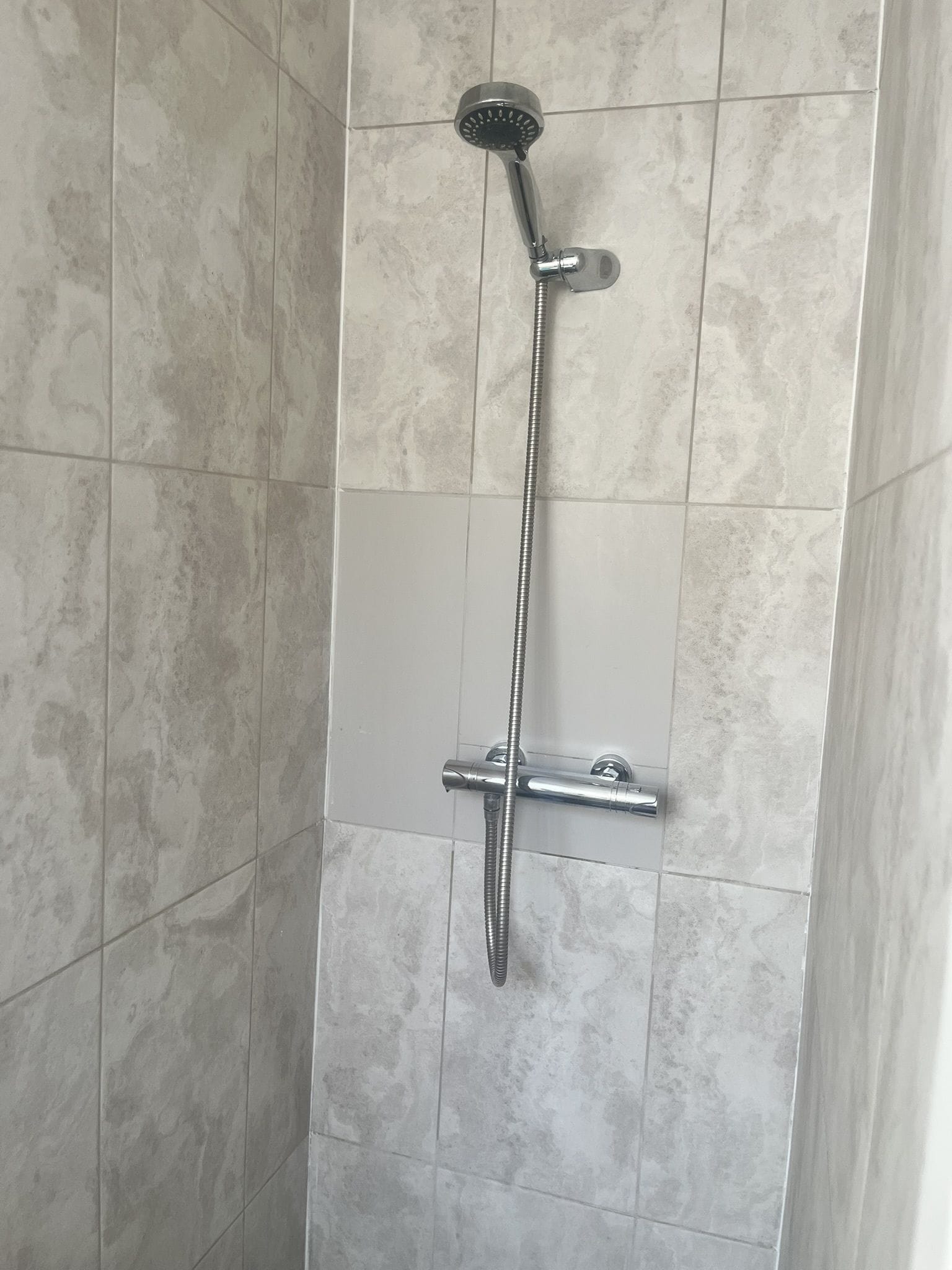 A shower with a handheld showerhead and a fixed wall-mounted faucet.