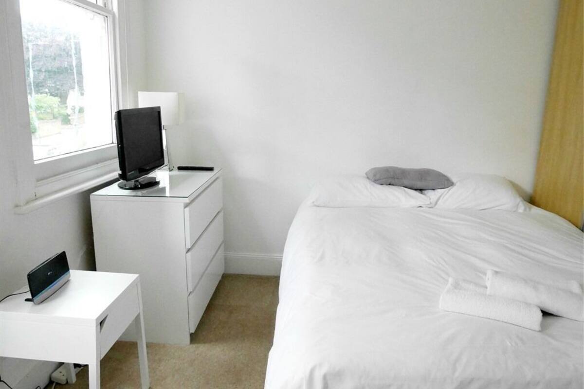 A bedroom with a bed, a desk with a computer, a television, and a window.