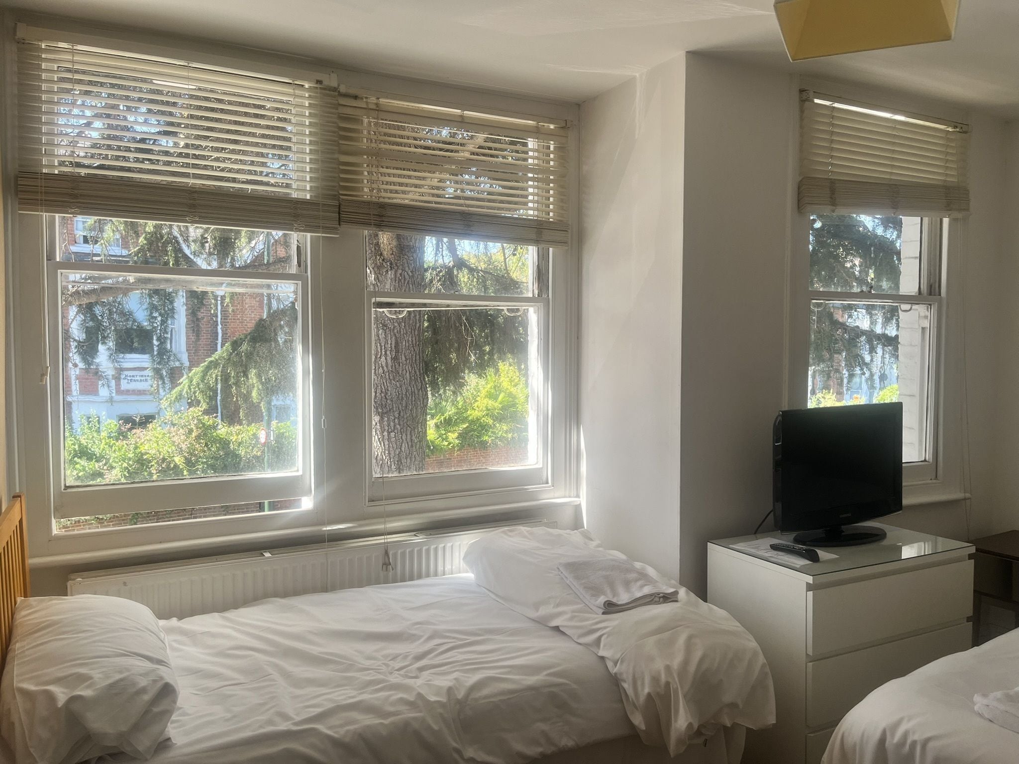 Un dormitorio con dos camas, un televisor sobre una cómoda y ventanas con persianas.