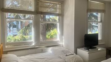 Un dormitorio con dos camas, un televisor sobre una cómoda y ventanas con persianas.