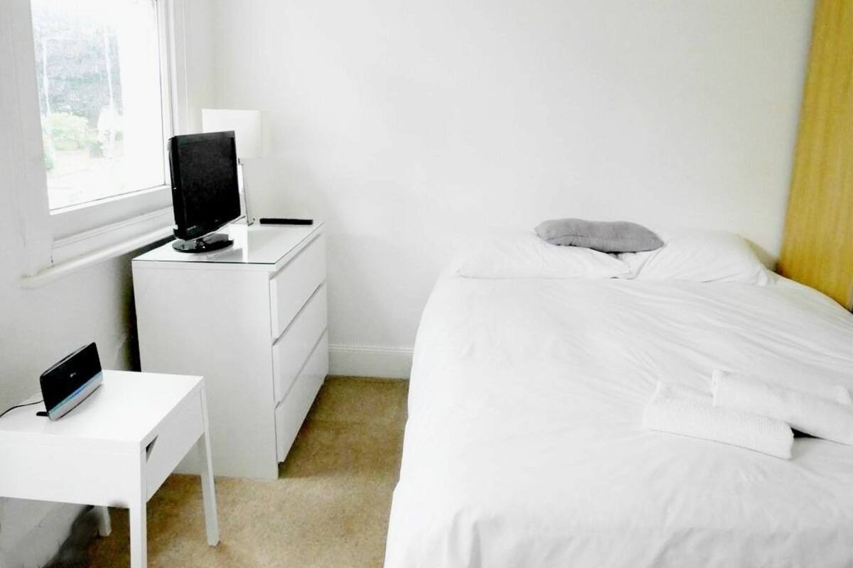 A bedroom with a bed, a desk with a computer, a TV, and a window.