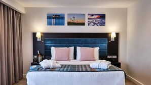 Un lit bien fait, avec une tête de lit bleue, deux tables de chevet avec des lampes et trois tableaux encadrés accrochés au mur.