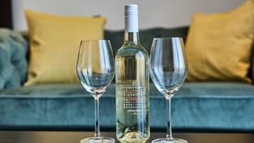 Una botella de vino y dos copas sobre una mesa frente a un sofá con cojines.