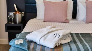 A neatly made bed with a striped blanket, a folded robe with a logo, and a minibar with a bottle and glasses.