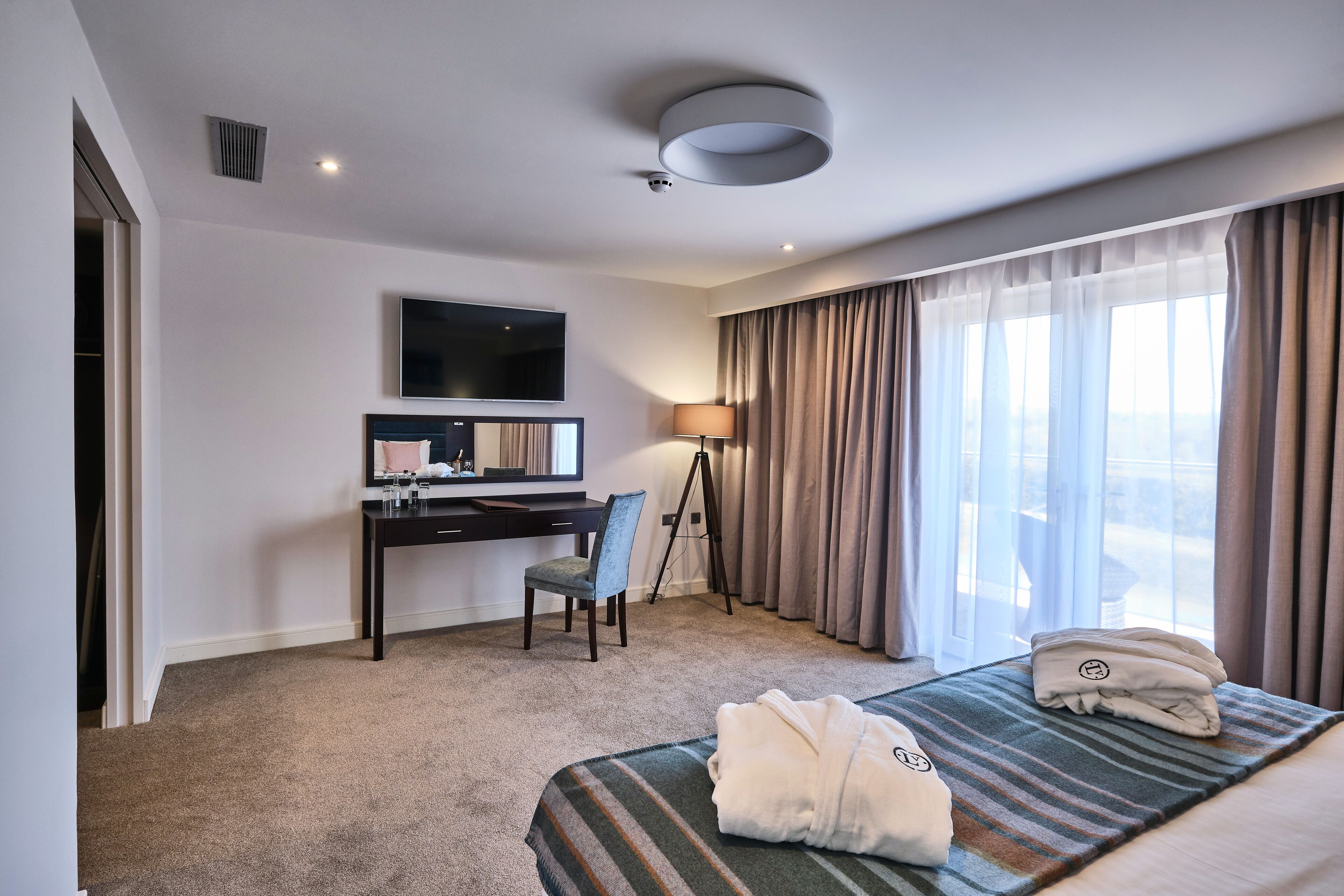 A hotel room with a bed, a desk, a chair, a television, and a window with curtains.