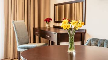 Una habitación de hotel con una mesa redonda, una silla, un jarrón con flores amarillas, un jarrón con flores rojas y un espejo grande en la pared.
