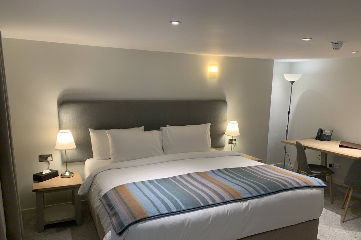 Habitación de hotel con una cama grande, dos mesitas de noche con lámparas, un escritorio con silla y un teléfono.