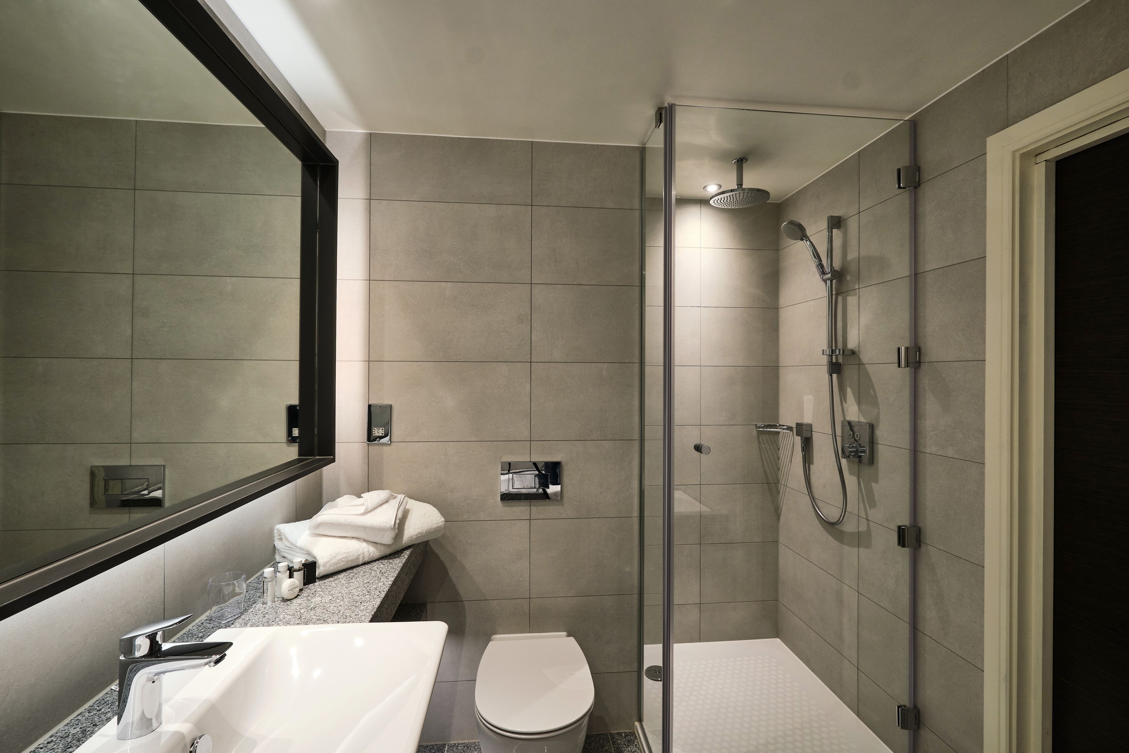 Un baño moderno con ducha de vidrio, inodoro blanco y lavamanos con espejo superior.
