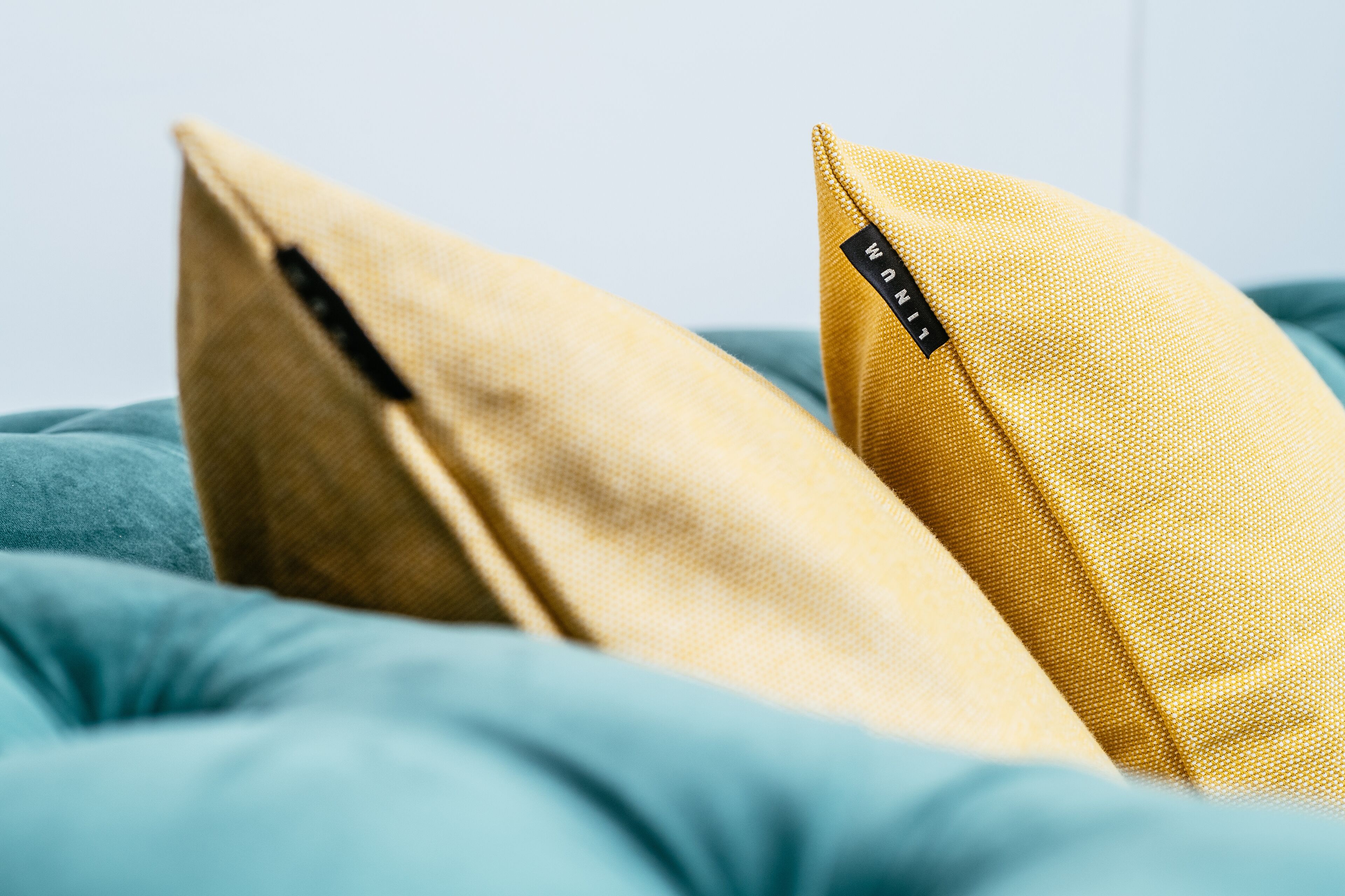 A bed with two pillows, one yellow and one beige, and a teal-colored blanket.