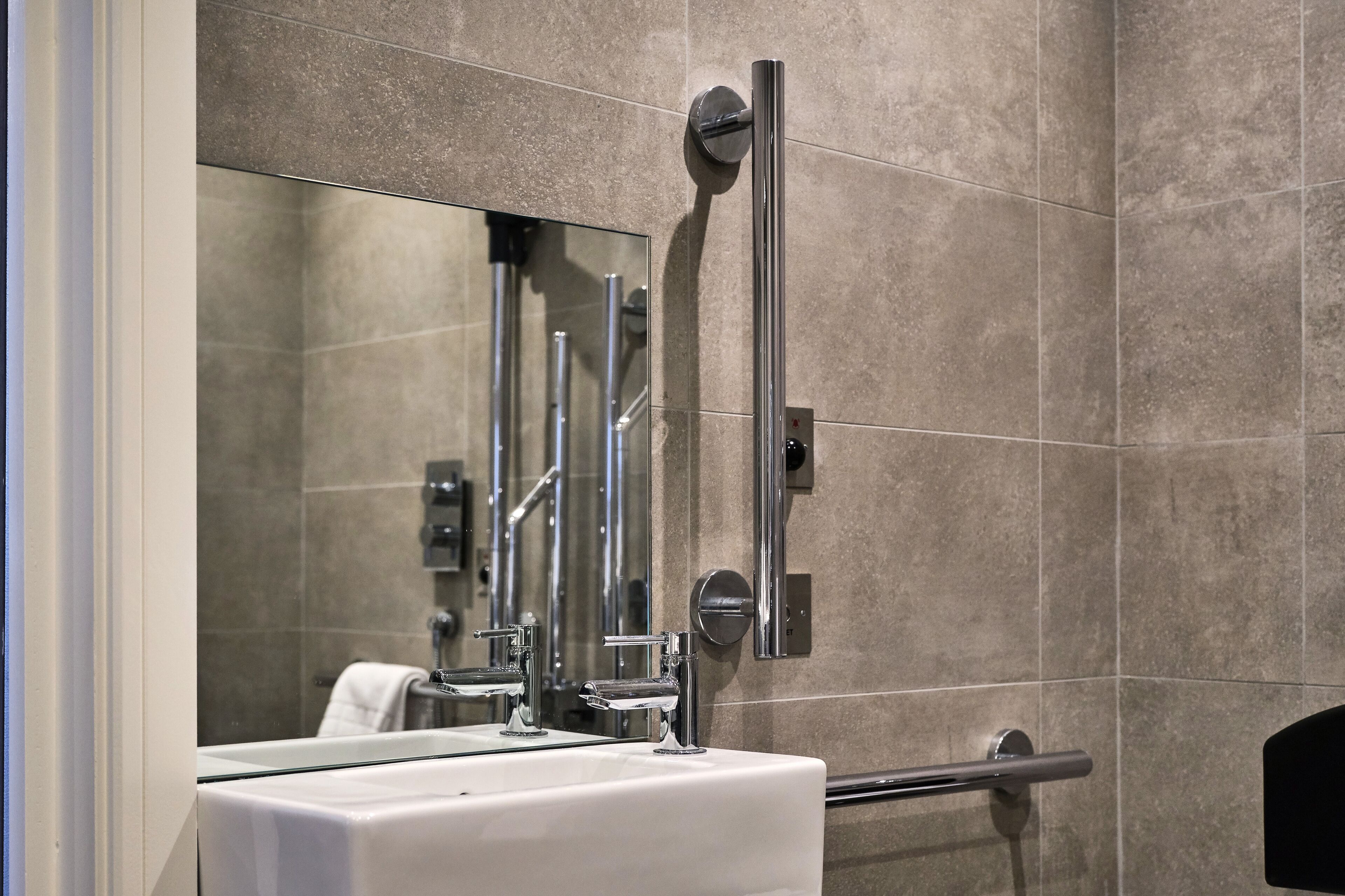 A modern bathroom with a large mirror, chrome fixtures, and a tiled wall.