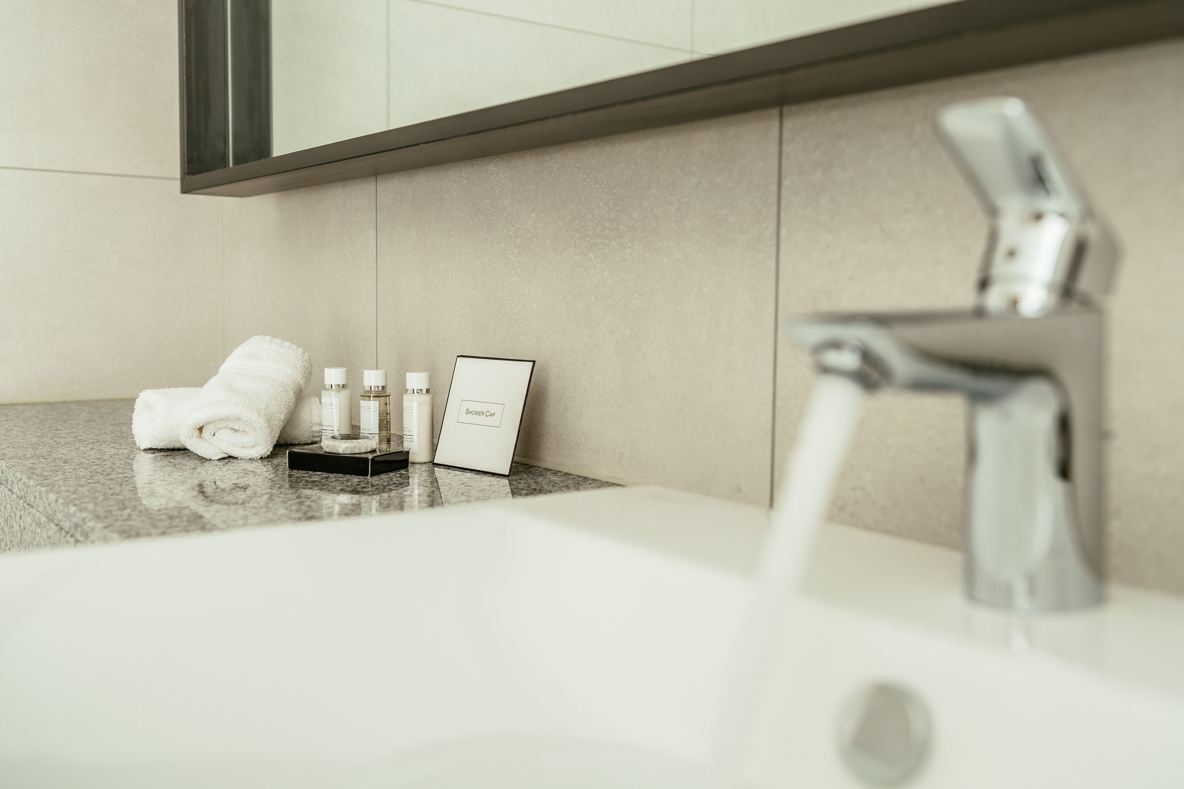A bathroom with a sink, running water, a towel, and toiletries.