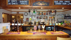 A bar with multiple beer taps, a clock, and a sign indicating free pool access on Sundays. - London Inn (Cheltenham)