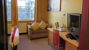 A hotel room with a bed, a sofa, a desk with a computer, a window with curtains, and a painting on the wall. - London Inn (Cheltenham)