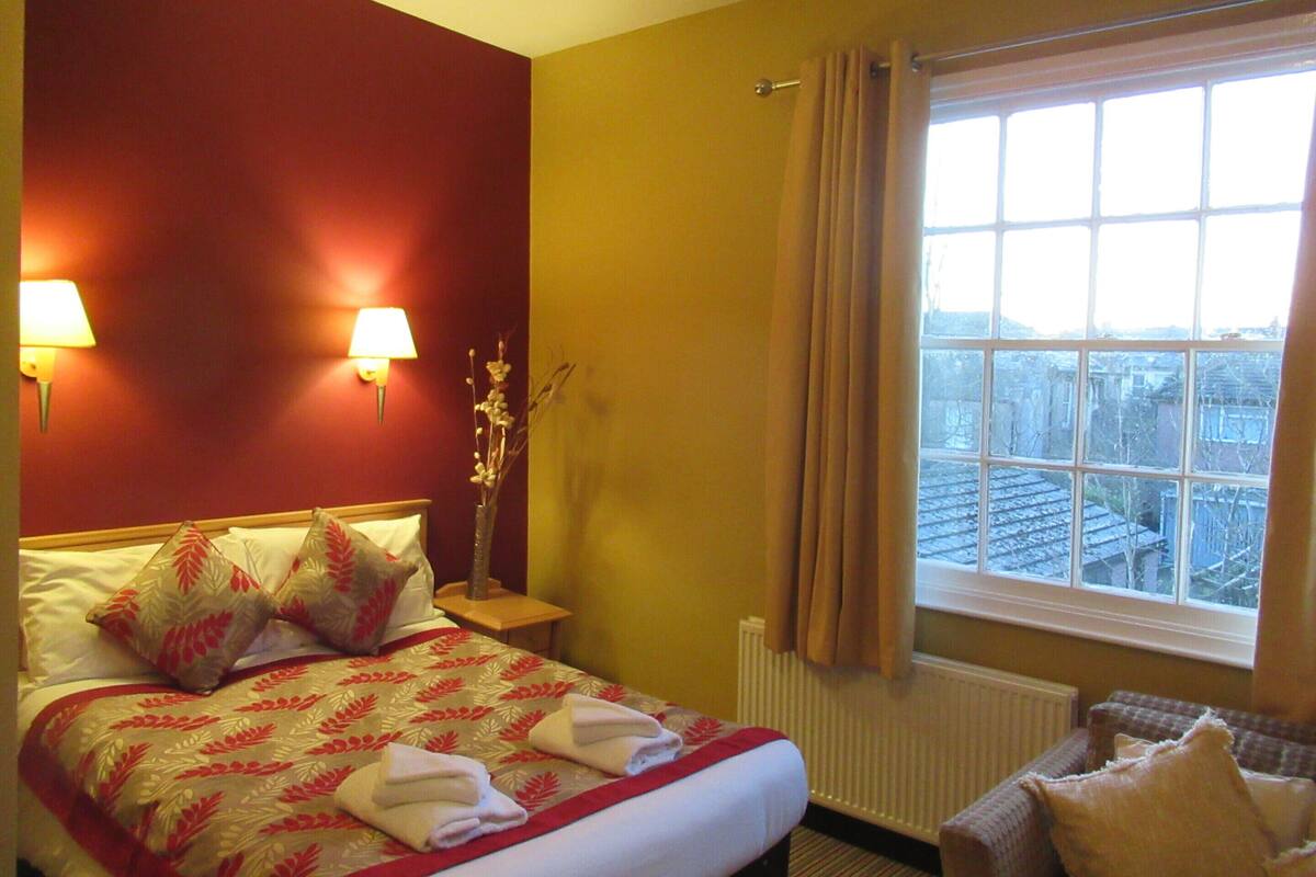 A hotel room with a bed, two bedside lamps, a window with curtains, and a view of the cityscape.