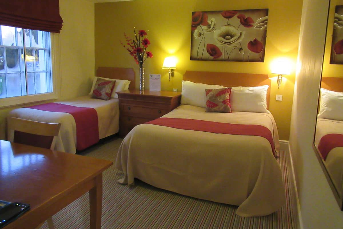 A hotel room with two beds, a desk, and a window.