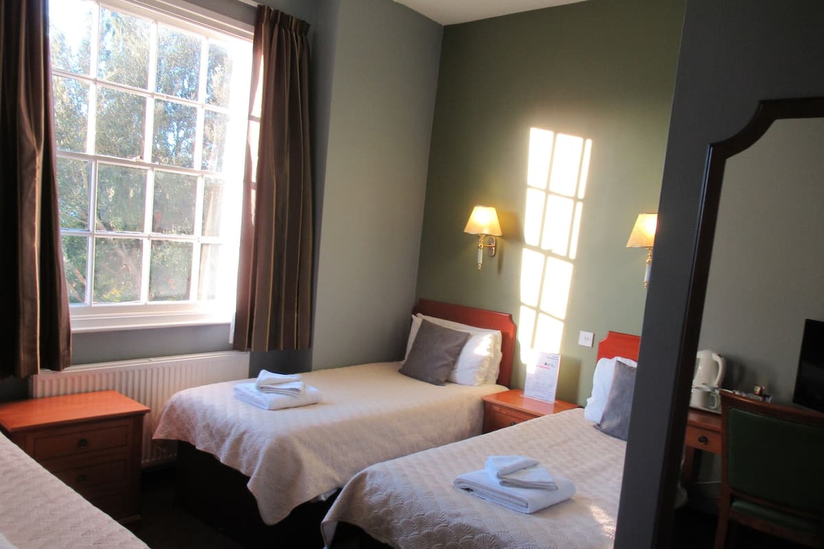 A hotel room with two beds, a window with curtains, a bedside lamp, and a mirror.