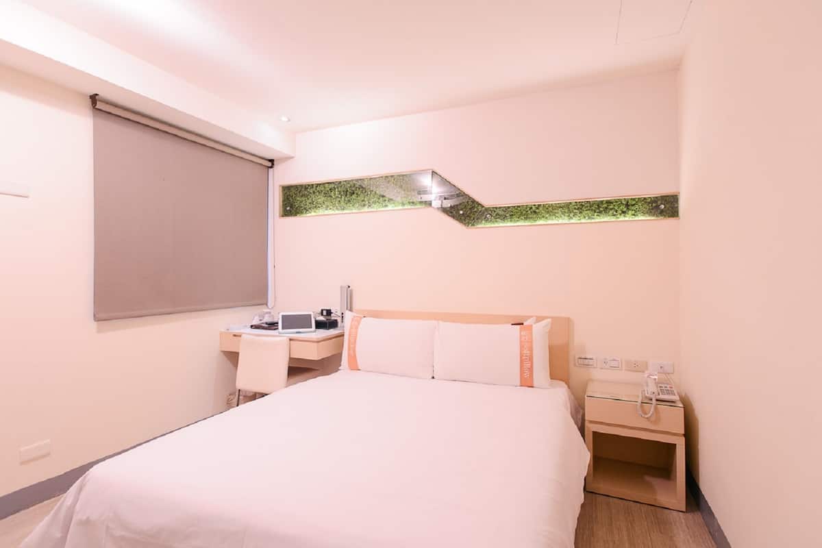 Ein Hotelzimmer mit Bett, Schreibtisch, Stuhl, Telefon und kleinem Tisch.