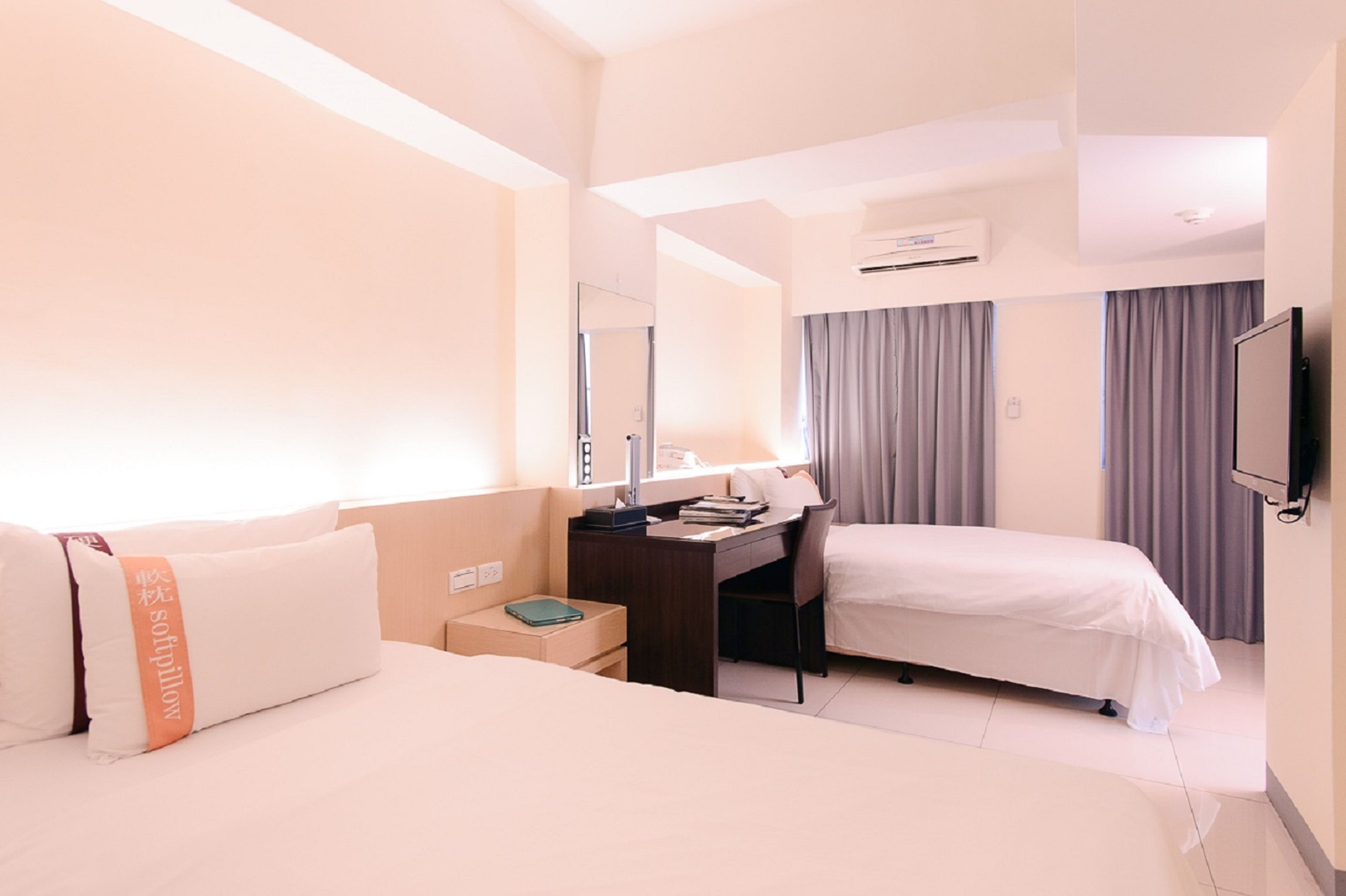 A hotel room with two beds, a desk, a chair, a TV, and an air conditioning unit.