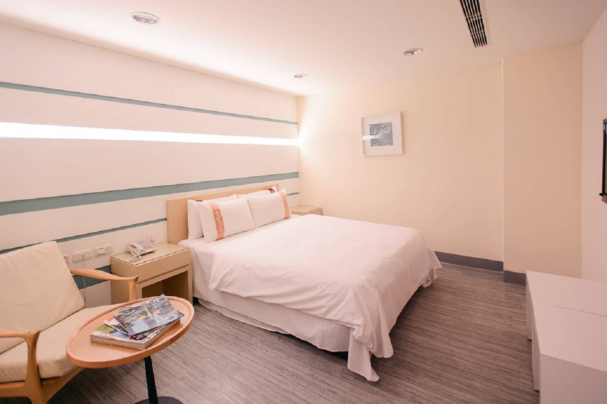 Ein Hotelzimmer mit einem Bett, Nachttisch, Stuhl und einem kleinen Tisch mit Zeitschriften.